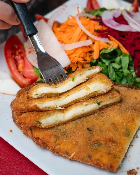 Milanesa de quesillo cortada, con el queso estirándose, y ensalada